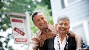 older couple next to for sale lawn sign